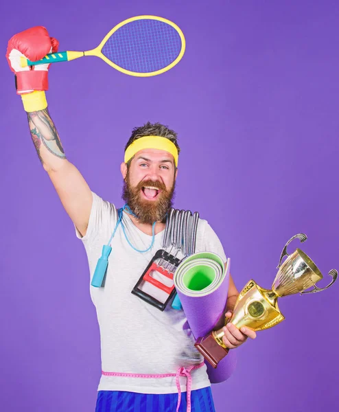 Choose favorite sport. Sport concept. On way to achievement. Sport shop assortment. Man bearded athlete hold sport equipment jump rope fitness mat boxing glove expander racket and golden goblet