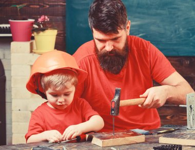 Çocuk, koruyucu kaskla meşgul olan çocuk babamla hobnails çekiçle vurmaya öğreniyor. Baba, sakallı veli küçük oğluna hobnails ve çekiç kullanmayı öğretiyor. Atölye ve tamirci konsepti