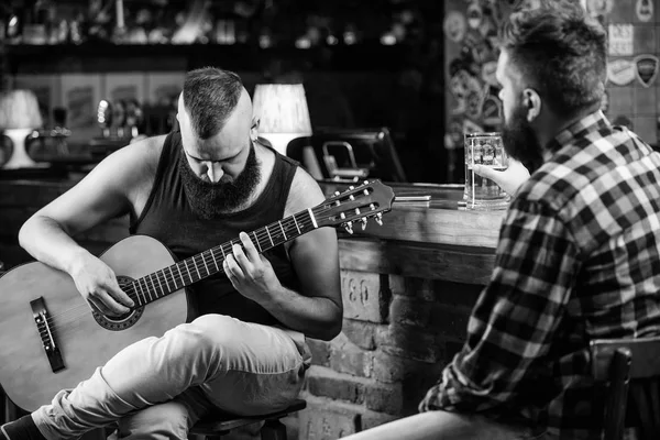 Friends relaxing in bar or pub. Hipster brutal bearded spend leisure with friend in bar. Real men leisure. Cheerful friends relax with guitar music. Man play guitar in bar. Friday relaxation in bar