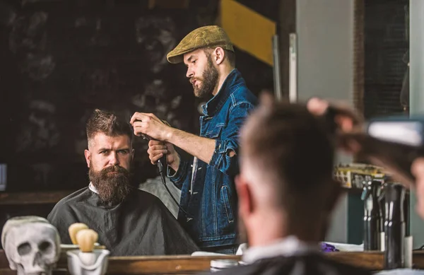 Hipster bearded client getting hairstyle. Barber with hairdryer works on hairstyle for bearded man, barbershop background. Styling concept. Barber with hairdryer drying and styling hair of client — Stock Photo, Image