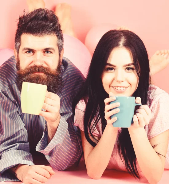 Paar entspannen am Morgen mit Kaffee. Familientradition. Mann und Frau auf lächelnden Gesichtern lagen auf rosa Hintergrund. Verliebte Paare trinken Kaffee im Bett. Mann und Frau in Hauskleidung, Schlafanzug — Stockfoto