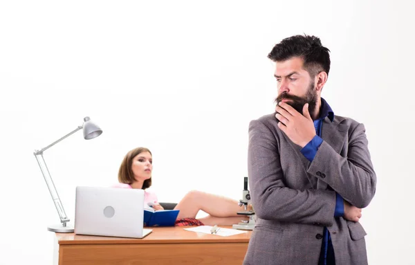Занятой человек. Уверенный бизнесмен и симпатичная секретарша в офисе. Бородатый мужчина смотрит на сексуальную женщину, работающую на заднем плане. Жестокий кавказский мужчина с длинной бородой в деловой одежде с коллегой — стоковое фото