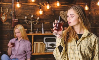 Rahat rahatlatıcı, defocused kareli giysiler yüzlerine arkadaşlar. Arkadaşlar sıcak bir atmosferde, ahşap iç mulled şarap tadını çıkarın. Rahatlatıcı ve mulled şarap içme kızlar. Dinlenmek ve rahatlamak kavramı