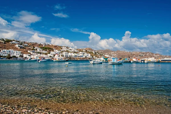 Fishing village beach in Mykonos, Greece. Sea and boats on cloudy blue sky. White houses on mountain landscape with nice architecture. Summer vacation on mediterranean island. Wanderlust and travel — Stock Photo, Image