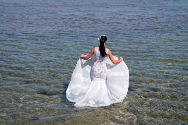 Gelin beyaz gelinlik deniz suyunda standı. Islı gelinlik sıcak güneşli bir gün. Gelin mutlu yaz tatili okyanus arka plan keyfini çıkarın. Deniz tatil beldesinde balayı. Yurt dışında düğün. Düğün töreni deniz kıyısı