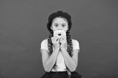 Resist taze yapılmış çörek için imkansız. Kız tatlı çörek elinde kırmızı camlı arka plan tutun. Çocuk gülümseyen kız donut yemeye hazır. Şeker dükkanı ve ekmek kavramı. Pişmiş çörekler çocuklar büyük hayranları