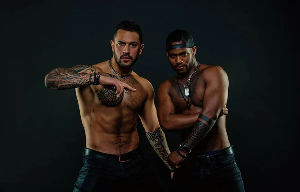 Men with fit tattooed bodies. African and hispanic men with sexy bare torsos. Fashion models with tattoo in jeans. Sportsmen with muscular chest and belly. Sport with fitness and bodycare — Stock Photo, Image