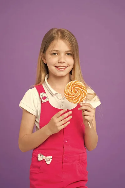 Versuchen Sie mein Lutscher kleines Kind lächelnd mit Zuckerstange auf lila Hintergrund. Mädchen lächeln mit Lutscher auf violettem Hintergrund. glückliches Kind mit wirbelndem Karamell. Essen und Dessert. Ernährung und Diät — Stockfoto