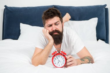 Yatakta depresif bir adam. zaman yönetimi. çalar saat ile yorgun sakallı adam hipster. yatak odasında acımasız uykulu adam. yatakta pijama sakallı olgun erkek. uykuda ve uyanık. enerji ve yorgunluk