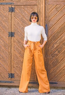 Kız makyaj moda giysiler içinde poz ile. Şık kıyafet ince uzun bayan. Moda ve stil kavramı. Kadın gevşek pantolon yürüyüş. Kadın moda esmer ayakta açık havada ahşap arka plan