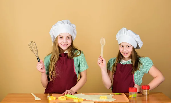 家族のレシピ。料理のスキル料理教育。生姜クッキーを焼く。女の子の姉妹は楽しい生姜生地を持っています。自家製クッキーが一番。子供たちは一緒にクッキーを焼きます。子供のエプロンとシェフの帽子の料理 — ストック写真