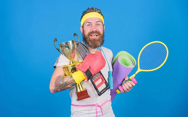 Man bearded athlete hold sport equipment jump rope fitness mat boxing glove expander racket and golden goblet. Choose sport you like. Sport concept. Sport shop assortment. Get body ready for summer — Stock Photo, Image