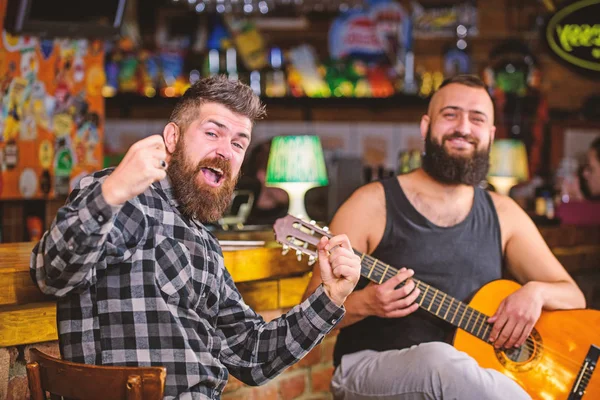Man play guitar in pub. Live music concert. Acoustic performance in pub. Hipster brutal bearded with friend in pub. Cheerful friends sing song guitar music. Relaxation in pub. Friends relaxing in pub