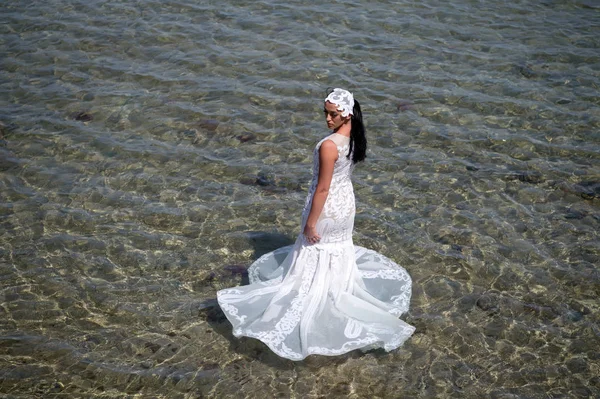 Boda en el extranjero. Ceremonia de boda a orillas del mar. Vestido de novia blanco de pie en agua de mar. Vestido de novia húmedo día soleado caliente. Novia feliz disfrutar de vacaciones de verano fondo océano. Luna de miel en el balneario — Foto de Stock