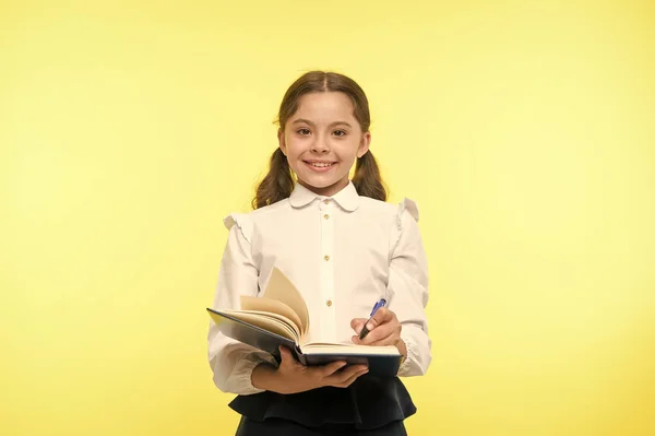 Escribe una nota para recordar. Niño escuela uniforme inteligente niño feliz tomar nota. Chica cara feliz tomar nota de la idea de fondo amarillo. Niña feliz escuela uniforme ropa sostiene libro listo escribir nota —  Fotos de Stock