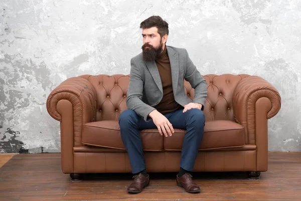 Realtor and rental service. Rent apartment. Bearded man with confident face sit leather couch. Loft interior apartment. Businessman realtor work. Furniture shop. Hipster realtor loft style apartment — Stock Photo, Image