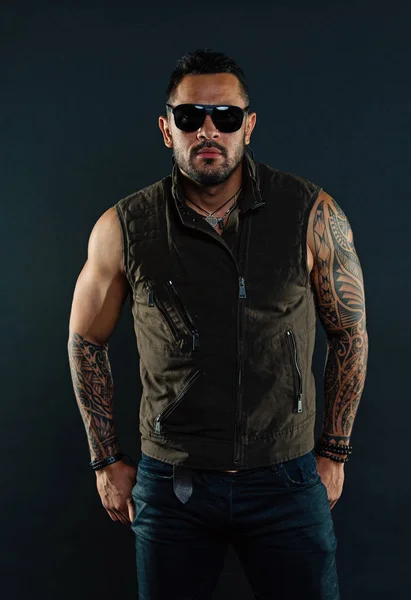 Fashion style and trend. Tattoo model with beard on unshaven face. Bearded man with tattoo on strong arms. Tattooed man with biceps and triceps. Fashion macho in trendy sunglasses