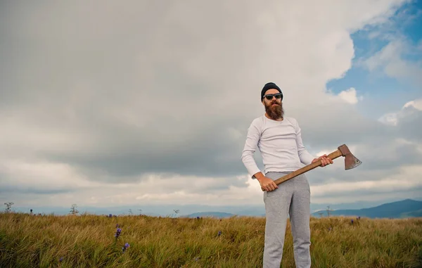 Hombre en gafas de sol con hacha de pie en el paisaje de montaña —  Fotos de Stock