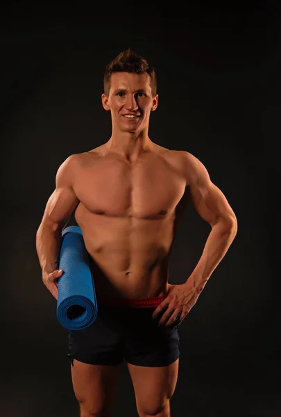 Sportman glimlach met sexy romp en zes pack. Gelukkig man houd yoga mat. Atleet glimlachend met sterke armen in korte broek. Fitnessapparatuur voor opleiding en training. Sport yoga en fitness activiteit — Stockfoto