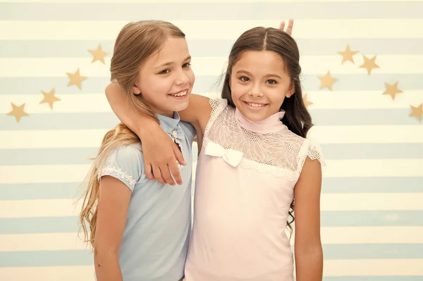 Girls children best friends hugs. Happy childhood concept. Kids schoolgirls preteens happy together. Friendship from childhood. Girls smiling happy faces hug each other while stand striped background