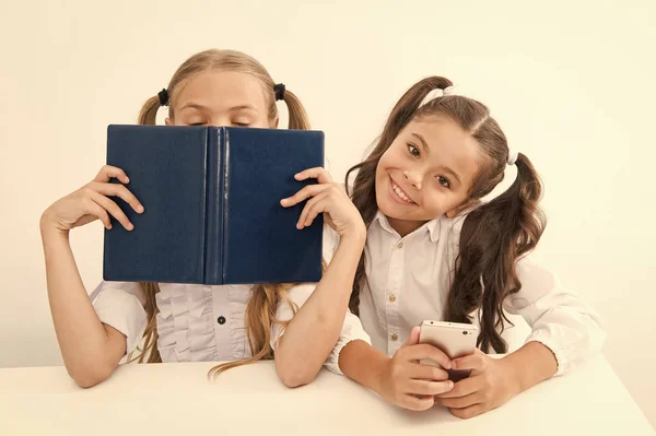 Velha escola contra o moderno. Schoolgirl segurar celular smartphone moderno, enquanto seu amigo desfrutar de livro antigo como armazenamento de dados analógicos. Tecnologia contra a experiência. Nova geração de demandas educacionais — Fotografia de Stock