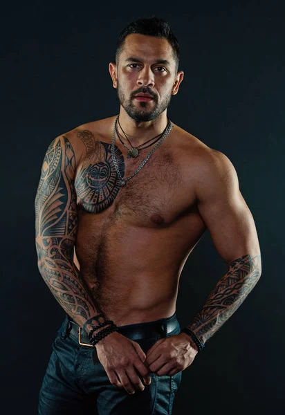 Uomo barbuto con corpo tatuato. Macho con torso nudo sexy in jeans. Modello tatuaggio con sei pack e ab. Atleta o sportivo con petto e pancia muscolosi. Sport o fitness e cura del corpo — Foto Stock