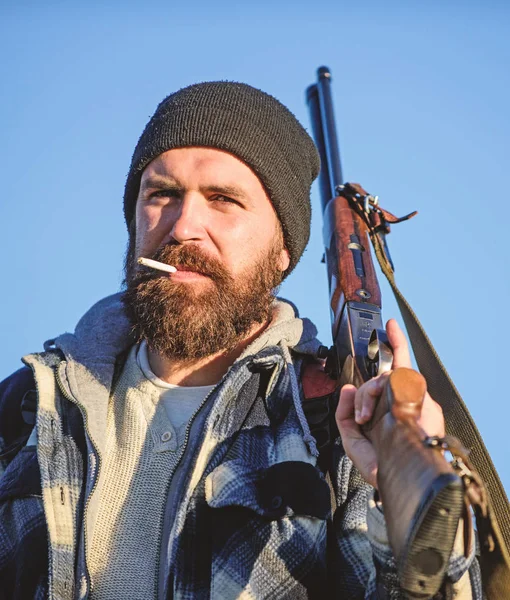 Caçador com espingarda de perto. Guy caçador barbudo passar a caça ao lazer e fumar. Caçando conceito de hobby masculino. Homem brutal barbudo cara gamekeeper azul céu fundo. Brutalidade e masculinidade — Fotografia de Stock