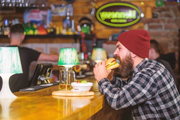 Man with beard eat burger menu. Brutal hipster bearded man sit at bar counter. High calorie food. Cheat meal. Delicious burger concept. Enjoy taste of fresh burger. Hipster hungry man eat burger