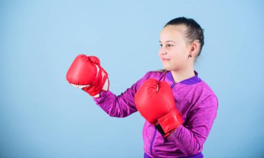 Klişenin aksine. Boks eldivenli boksör çocuk. Kendine güvenen bir genç. Spordan zevk. Kadın boksör. Spor terbiyesi. Boks sıkı disiplin sağlar. Mavi arka plan üzerinde kız sevimli boksör