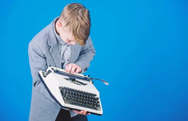 Usando una máquina de escribir. Escribir a máquina de escribir para niños pequeños. Elegante colegial con máquina de escribir vintage. Lindo chico con máquina de escribir. Niño sosteniendo la máquina de escribir retro sobre fondo azul, espacio para copiar — Foto de Stock