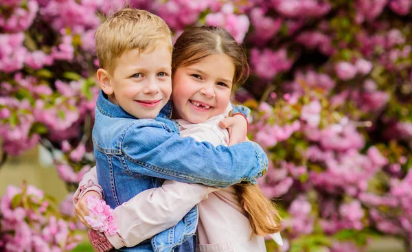 愛は空中にある。ロマンチックな赤ちゃんカップルの子供たちは桜の木の庭を歩きます。優しい愛の気持ち。小さな女の子と男の子ロマンチックなデート恋に落ちる春。愛ピンクの桜の子供たち — ストック写真