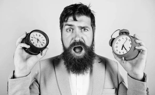 Cambia el reloj y arruina tu salud. El hombre barbudo hipster sostiene dos relojes diferentes. Tipo sin afeitar desconcertado cara tener problemas con el cambio de tiempo. Los cambios en las zonas horarias afectan la salud. Zona horaria — Foto de Stock