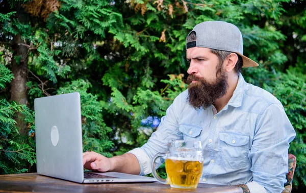 Bearded hipster freelancer enjoy end of working day with beer mug. Beer helps him relax after hard day. Brutal man leisure with beer and laptop. Finally friday. Hipster relax sit terrace with beer