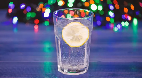 Detox after winter party. Health care concept. What to drink on christmas party. Cocktail glass with water and slice of lemon defocused garland lights. Detox drink to feel better. Hangover and detox — Stock Photo, Image