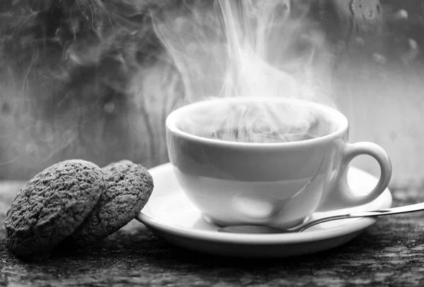 Coffee time on rainy day. Fresh brewed coffee in white cup or mug on windowsill. Wet glass window and cup of hot caffeine beverage. Coffee drink with oat cookies dessert. Enjoying coffee on rainy day