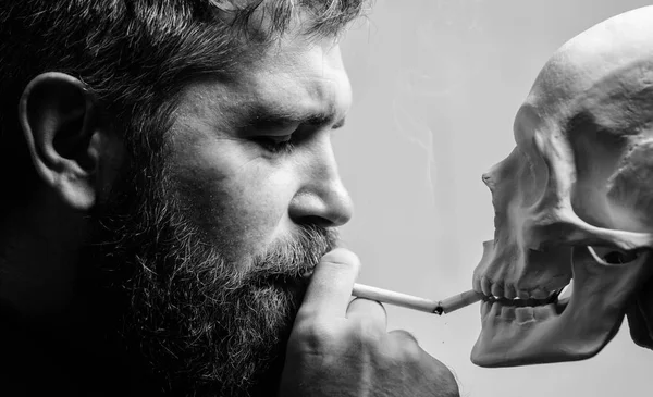 Smoking cause health damage and death. Man smoking cigarette near human skull symbol death. Nicotine destroy health. Harmful habits. Smoking is harmful. Habit to smoke tobacco bring harm to your body