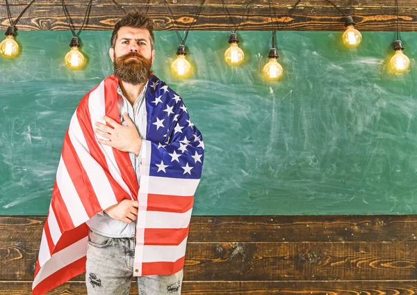 Concepto de educación patriótica. Profesora americana cubierta con bandera americana. Hombre con barba y bigote en cara seria con bandera de USA, pizarra de fondo. Profesor enseña a amar la patria, EE.UU. — Foto de Stock