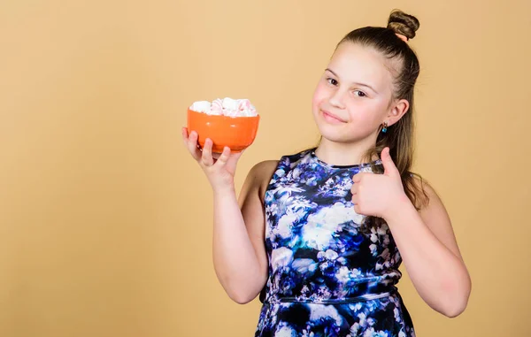 Meisje glimlachend gezicht houden Bowl met zoete marshmallows in hand beige achtergrond. Zoetekauw concept. Kid meisje met lang haar houdt van snoep en traktaties. Calorie en dieet. Hongerig kind. Marshmallow Challenge — Stockfoto