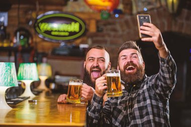 Çevrimiçi iletişim. Sakallı hippi adam akıllı telefon tutar. Selfie konseptini alıyorum. Barda harika bir akşam geçirdiğini hatırlamak için selfie çek. Arkadaşların sosyal ağlarına selfie çek. Barda bira içen bir adam