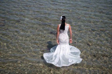 Deniz tatil beldesinde balayı. Yurt dışında düğün. Düğün töreni deniz kıyısı. Gelin beyaz gelinlik deniz suyunda standı. Islı gelinlik sıcak güneşli bir gün. Gelin mutlu yaz tatili okyanus arka plan keyfini çıkarın