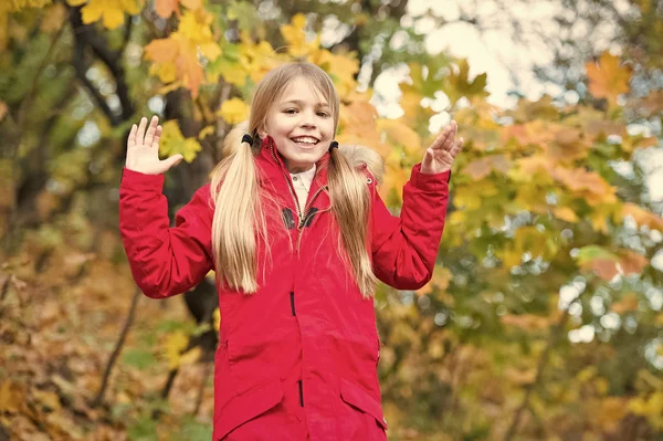 Una scolaretta allegra. Capelli lunghi biondi bambino che camminano in giacca calda all'aperto. Ragazza felice in cappotto rosso godere di autunno parco naturale. Bambino indossare cappotto alla moda con cappuccio. Autunno vestiti e concetto di moda — Foto Stock