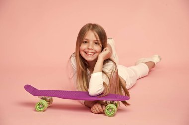 Beyaz kıyafeti yerde yatarken evlat. Uzun sarı saçları, pembe arka plan izole kız. Menekşe kaykay üzerinde yaslanmış şirin gülümseme ile çocuk. Genç gevşeme kavramı eğleniyor