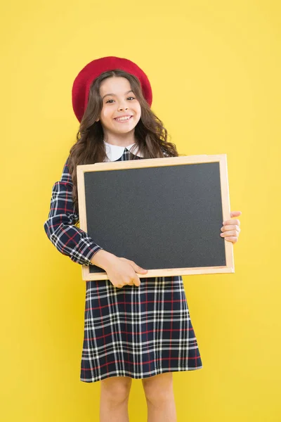 黄色のパリの子供。スペースをコピーします。空の黒板を持つ子供。ベレーで長い巻き毛を持つ幸せな女の子。広告。フランスのベレーの小さな女の子。インフォメーションボード。ここに有用な情報があります — ストック写真
