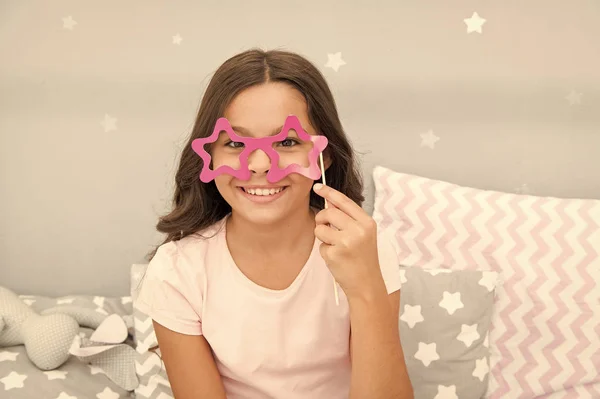 Slumber party photo booth props. Kid girl cheerful posing with star shaped eyeglasses party attribute. Prepare photo booth props hand made or buy for party. Printable photo booth props pajama party