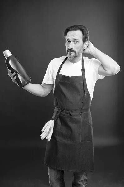 Man in apron with gloves hold plastic bottle liquid soap chemical cleaning agent. Cleaning day today. Bearded guy cleaning home. On guard of cleanliness and order. Cleaning service and household duty