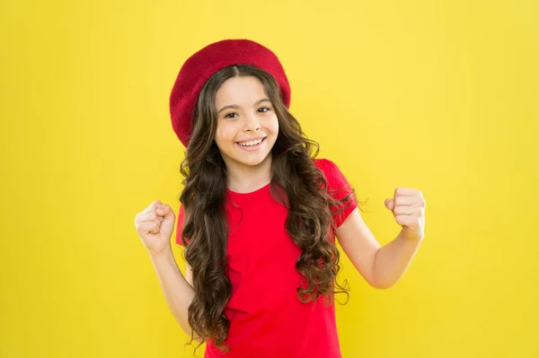 Geluk en mooi. Jongen meisje lang gezond glanzend haar draagt rode hoed. Klein meisje met lang haar. Kind blij schattig gezicht schattig krullend haar gele achtergrond. Schoonheidstips voor netjes haar. Glimlachend kind — Stockfoto