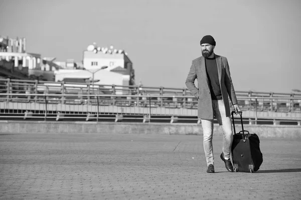 Hipster ready enjoy travel. Carry travel bag. Man bearded hipster travel with luggage bag on wheels. Traveler with suitcase arrive airport railway station urban background. Moving to new city alone