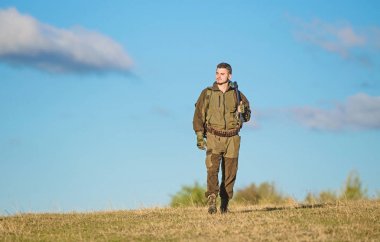 Doğayı avlayan adam. Erkeksi hobi aktivitesi. İnsan avcısı, mavi gökyüzü arka planında tüfek taşır. Tecrübe ve pratik, avlanmayı başarıya ulaştırır. Av silahı ya da tüfek. Avcılık hobisi