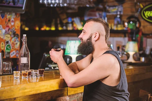 Hipster hombre brutal bebiendo alcohol pidiendo más bebidas en el mostrador del bar. El tipo pasa el tiempo libre en el bar con alcohol. Un borracho se sienta solo en el pub. Alcoholismo y depresión. Concepto adicto al alcohol —  Fotos de Stock