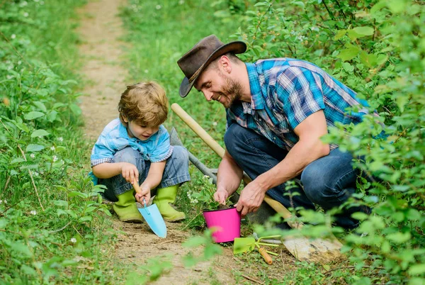 Gardening hobby. Dad teaching little son care plants. Spring gardening routine. Planting flowers. Little helper in garden. Farm family. Little boy and father in nature background. Gardening tools